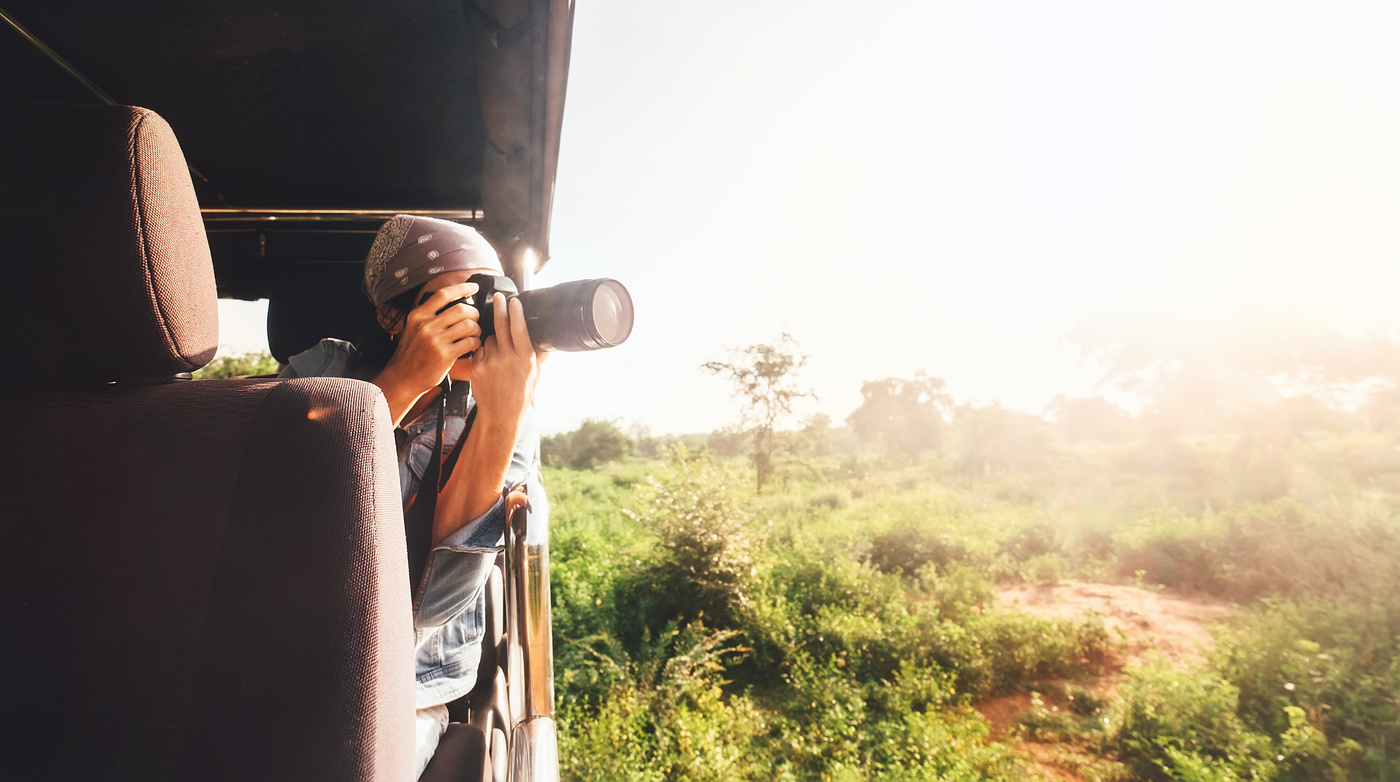 Woman photographer takes a picture with professional camera from touristic vehicle on tropical safari